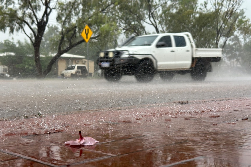 Heavy rain falls on a ute as it drives along a road
