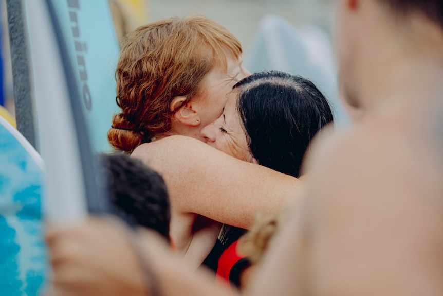 Two women hugging amongst a crowd of people with boards.