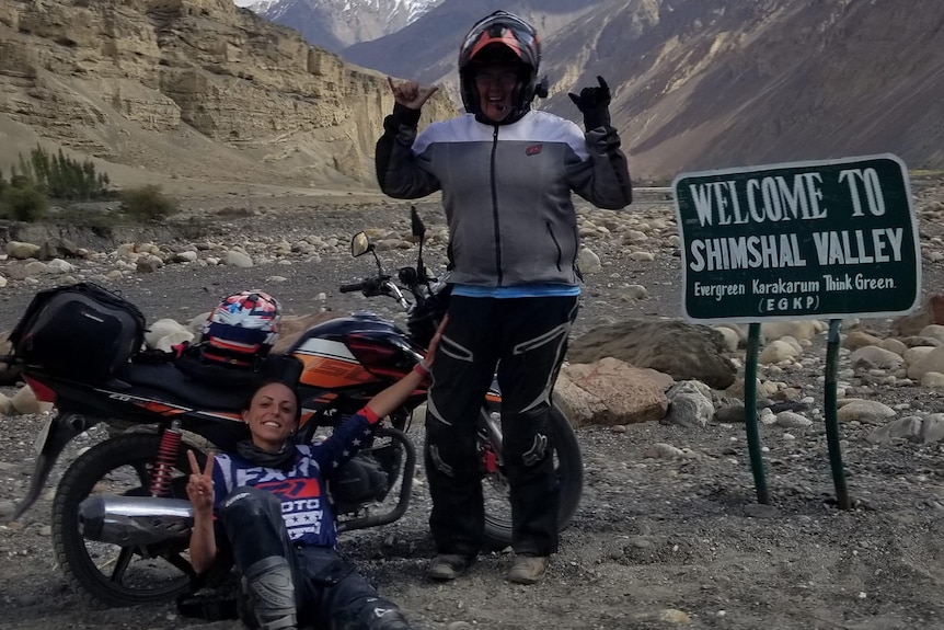 Two women celebrate next to a sign for the Shimshal Valley.