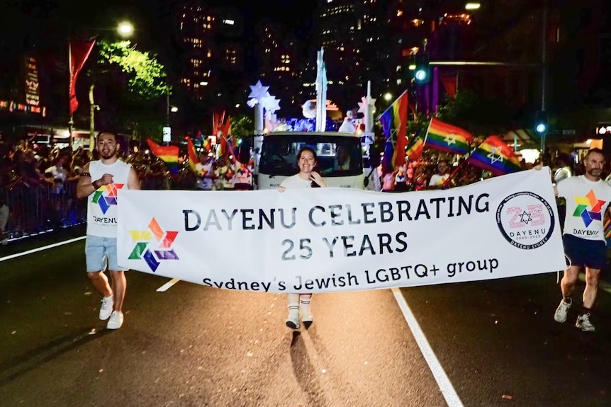 people marching at mardi gras parade behing a banner that reads dayenu celebrating 25 years