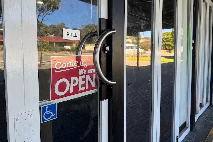 A sign saying 'come in, we are open', hung on a glass store door. 