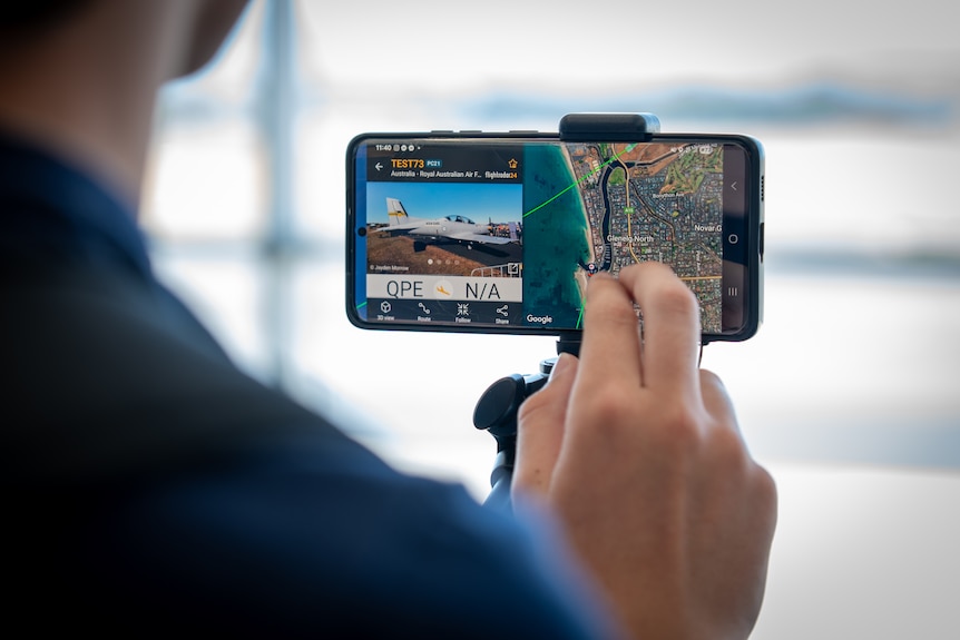 Fingers using a smartphone showing a map and a picture of a plane