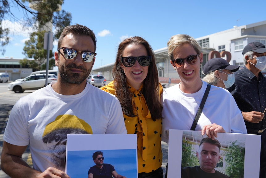 Three people stand with two photos of portraits of fmaily members. 