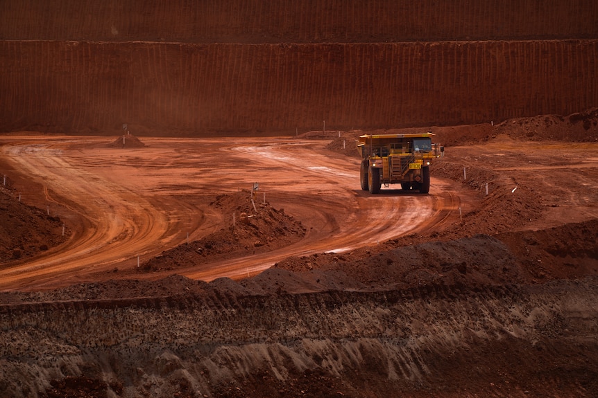Heavy vehicle collecting earth from a mine site driving on red dirt.