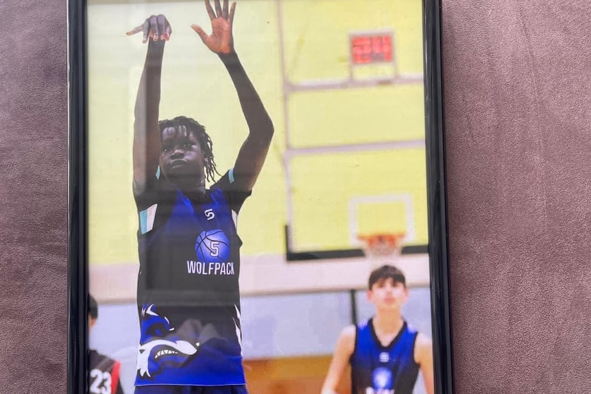 A framed photo of a young African teen shooting a goal in basketball. 