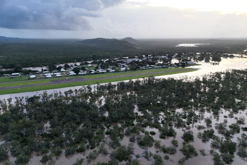 Floodwaters encroaching near a remote town, in a lush green landscape.