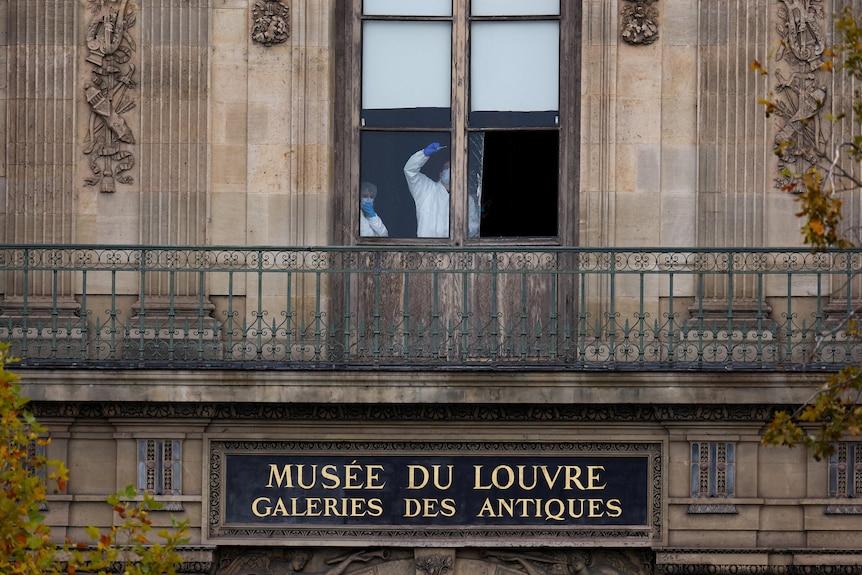 A person in a white hazmat suit and blue hair net cleaning a window.