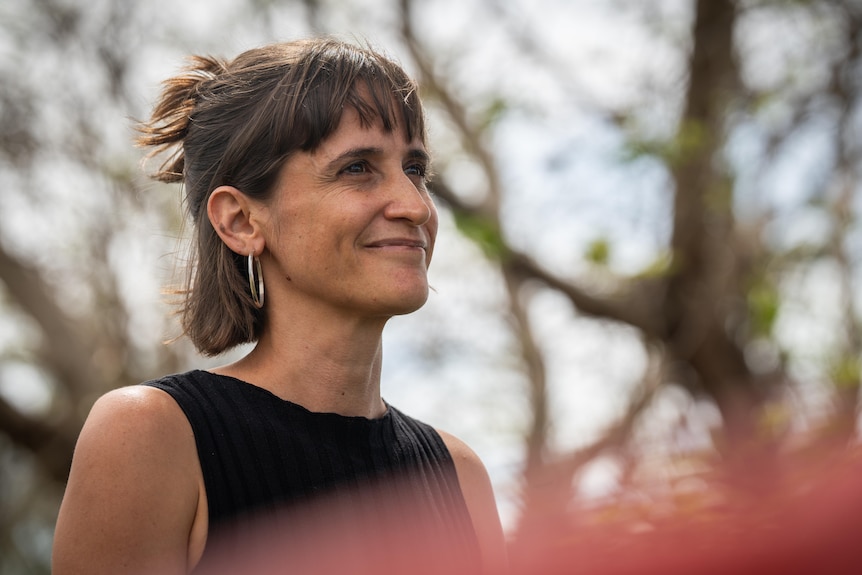 Woman in black top and large earing smiles with mouth closed