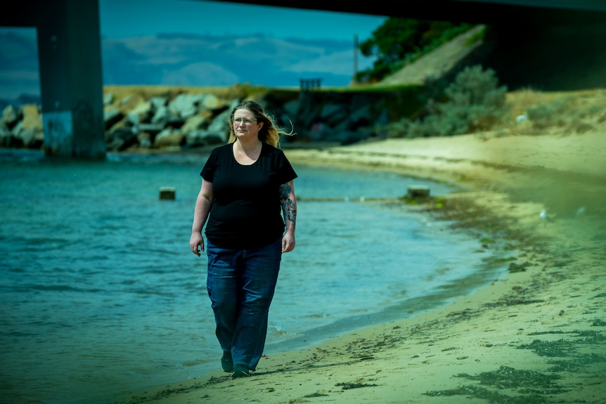 A woman walks on the water's edge on a beach.