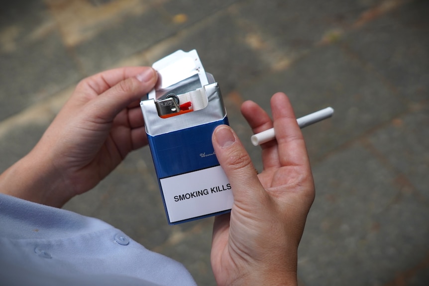 Woman holds packet of illegal cigarettes and lighter.