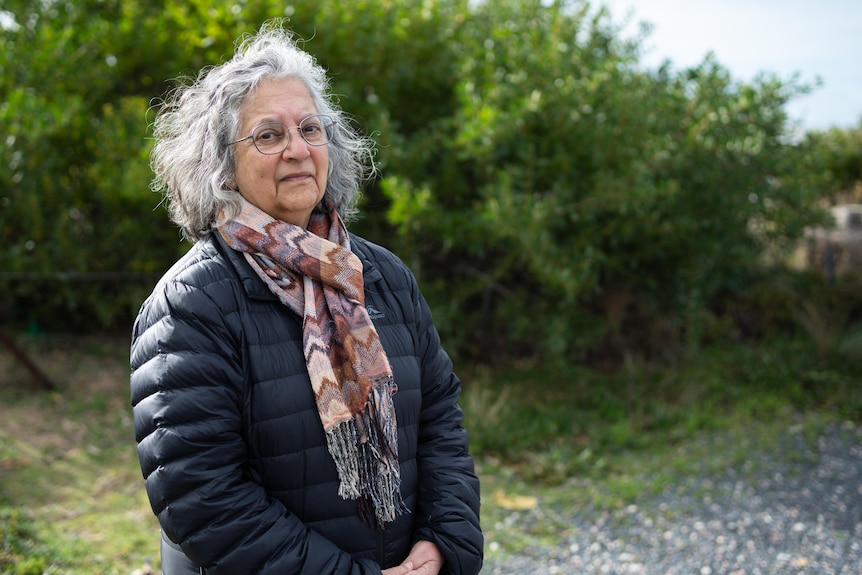 Perviz Marker, an older woman in a puffer jacket, is standing outside.