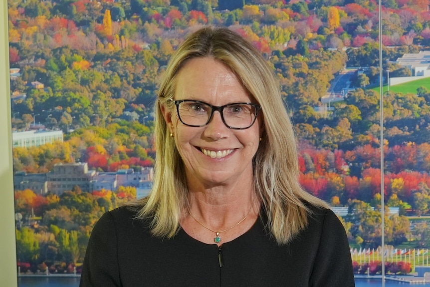 A woman with blonde hair and glasses smiles at the camera.
