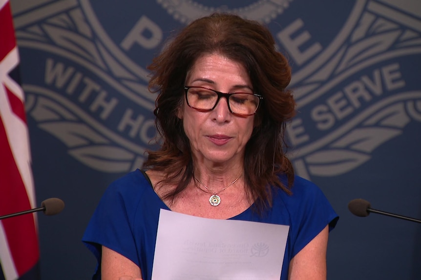 A woman in a blue dress and glasses reading a statement at a police press conference