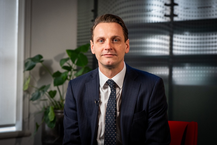 A man in a blue suit and tie looks at camera.