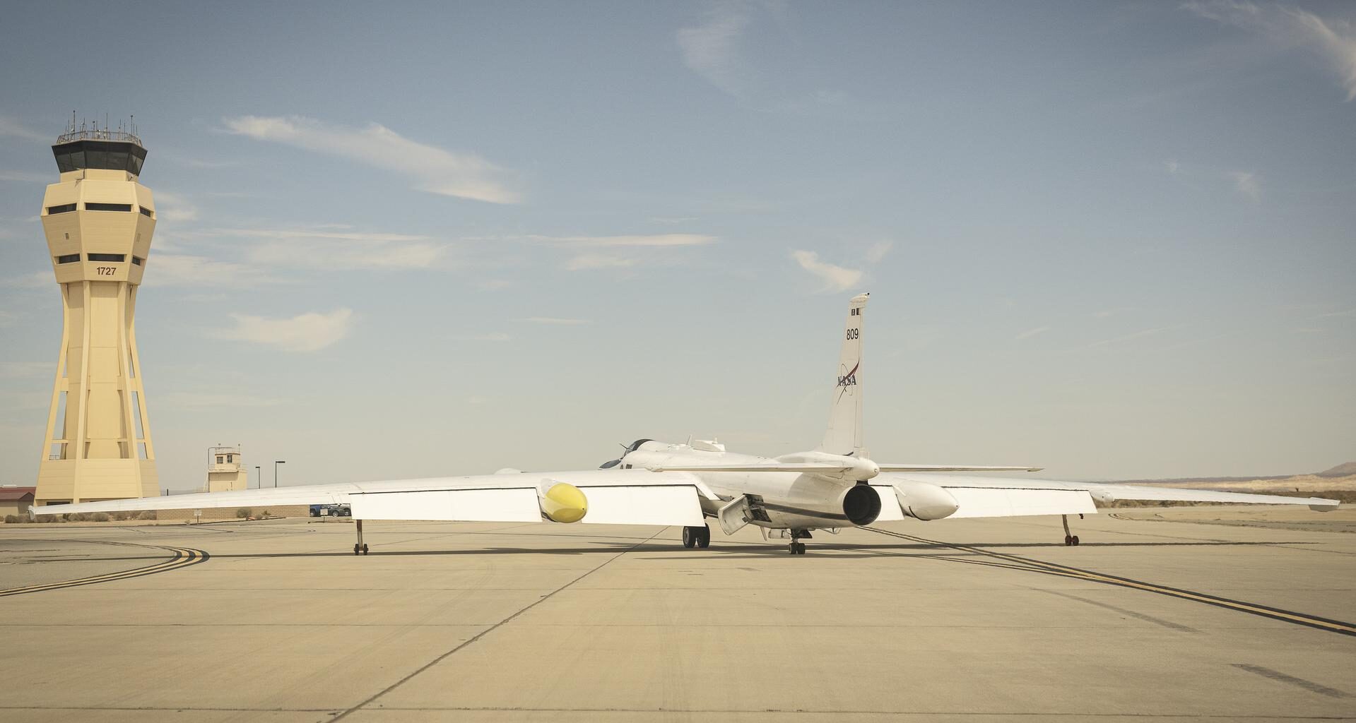 A NASA ER-2 aircraft taxis on the runway at Armstrong Flight Research Center with the control tower in the background.