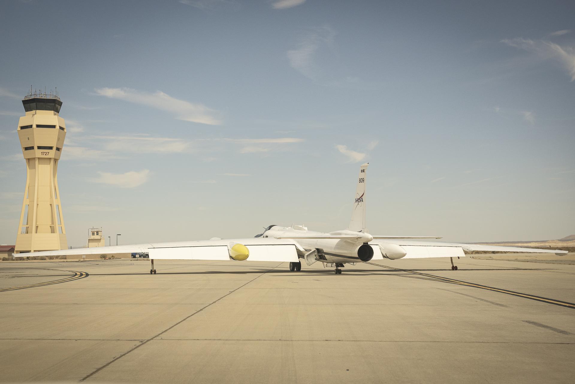 A NASA ER-2 aircraft taxis on the runway at Armstrong Flight Research Center with the control tower in the background.