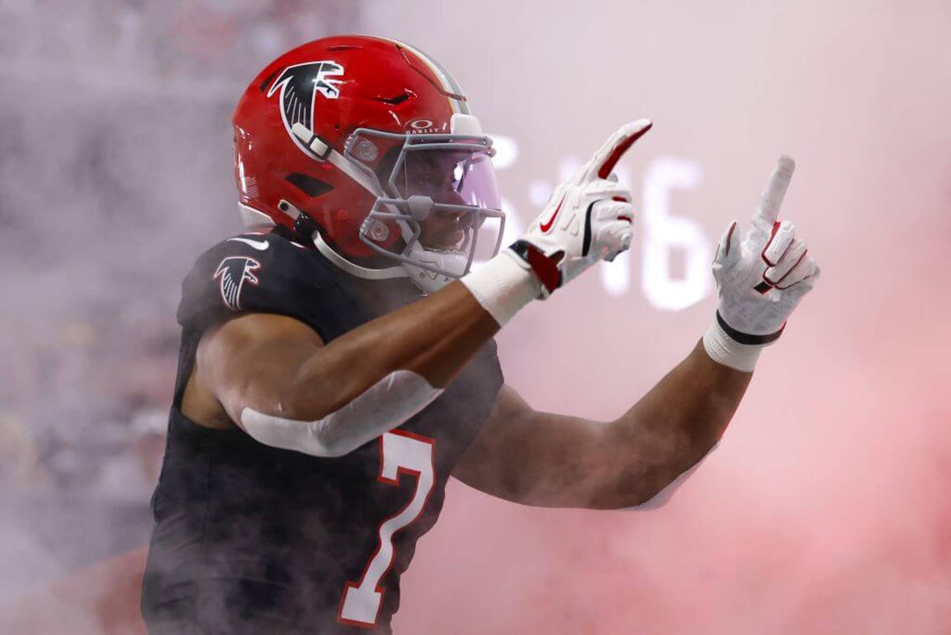 Atlanta's Bijan Robinson, donning a black Falcons jersey and red helmet, emerges from the smoke of pre-game introductions with both arms extended and index fingers pointing up.