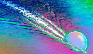 A colorful image shows a opalescent sphere carving a streak through a rainbow colored surface, kicking up white streaks behind it