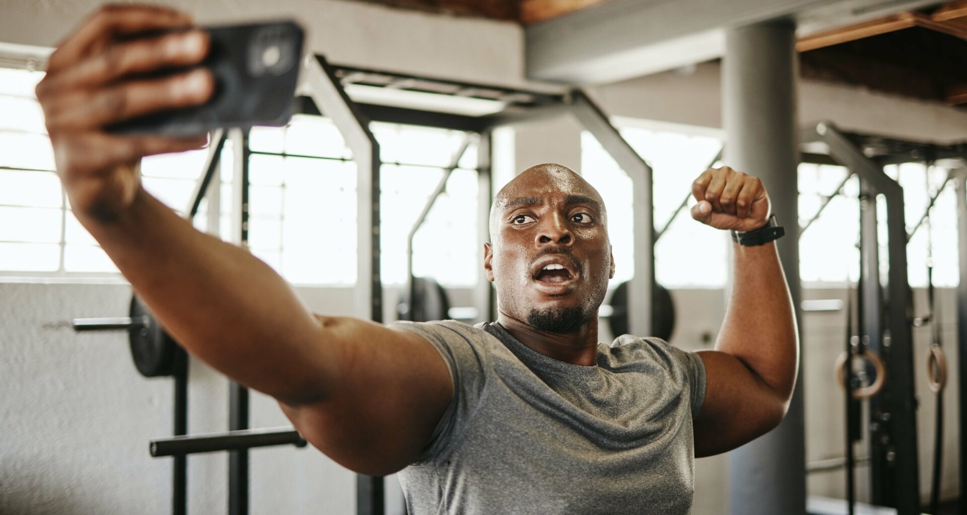 Gym selfie, smartphone and man flexing arm muscle for a post gyming pump bodybuilding exercise for online social media.