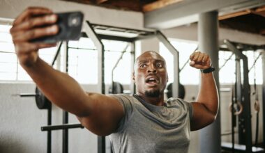 Gym selfie, smartphone and man flexing arm muscle for a post gyming pump bodybuilding exercise for online social media.