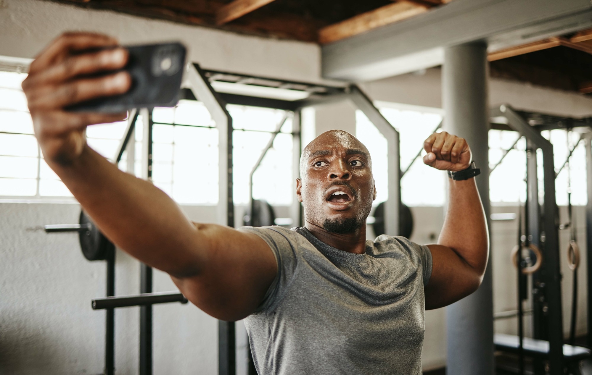 Gym selfie, smartphone and man flexing arm muscle for a post gyming pump bodybuilding exercise for online social media.