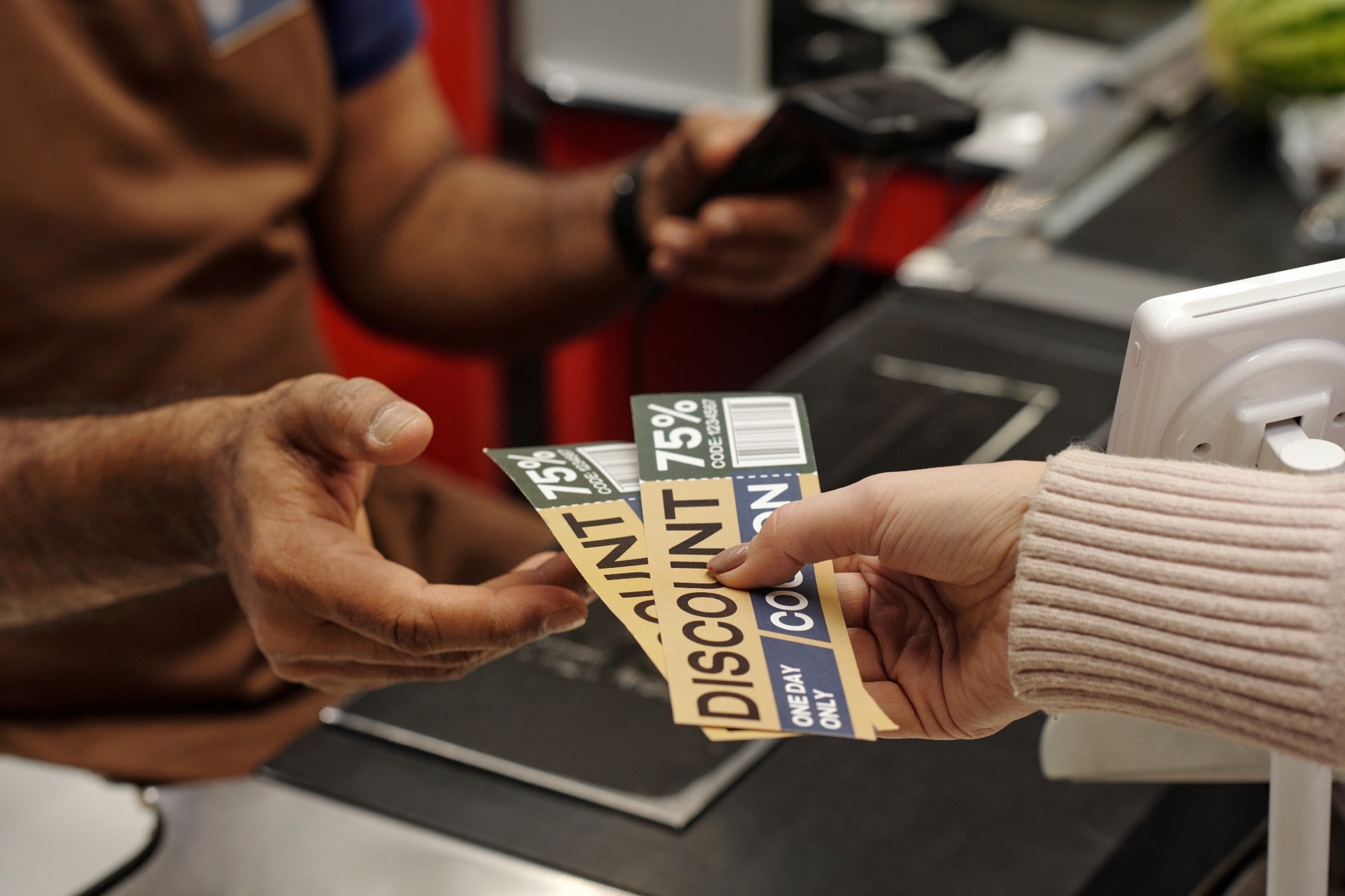 Closeup of female hand holding discount coupons for best deals and giving to cashier at supermarket checkout line