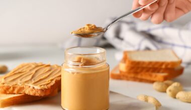Female hand with jar of tasty peanut butter, spoon and toasts on white background