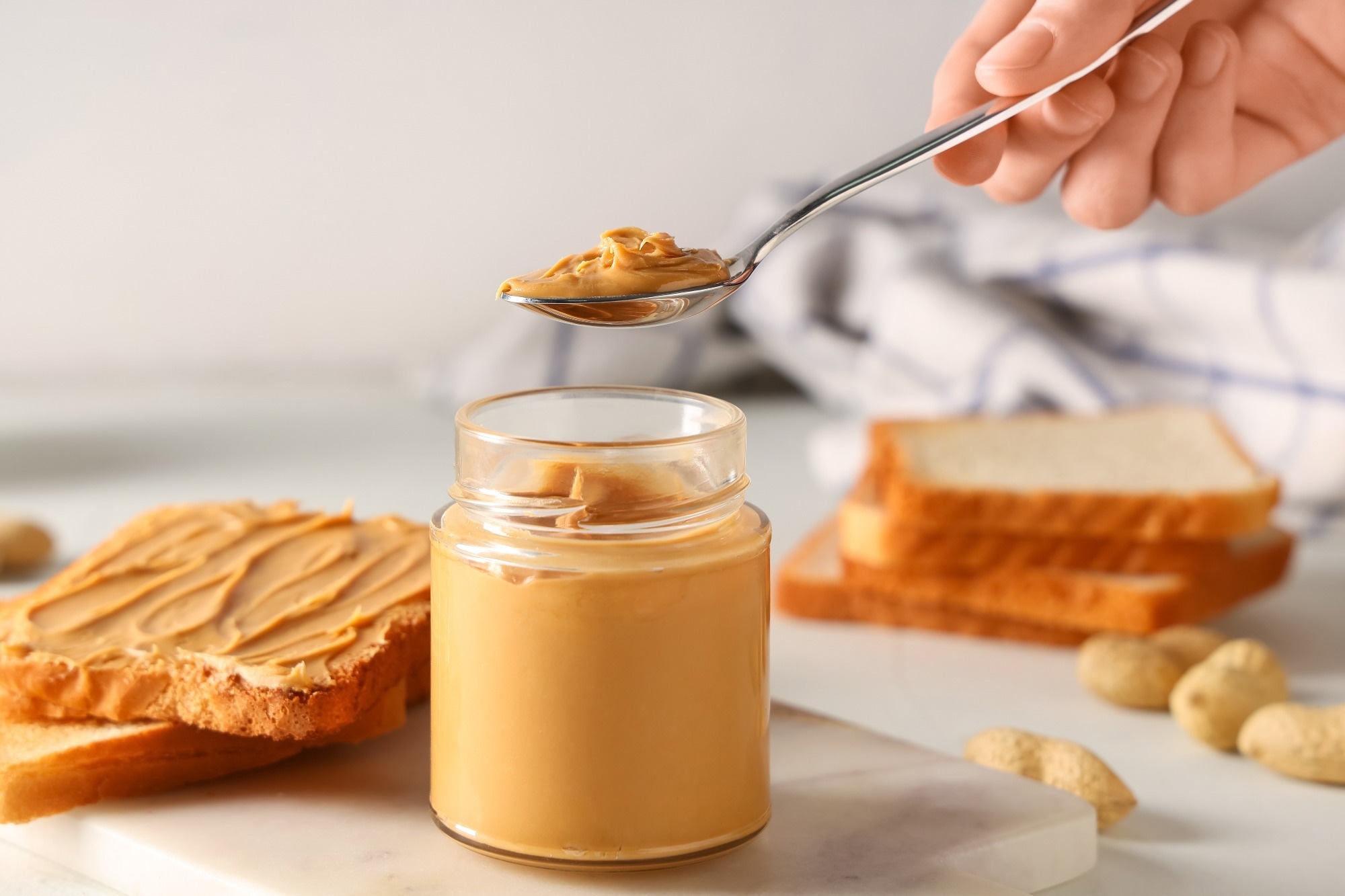 Female hand with jar of tasty peanut butter, spoon and toasts on white background
