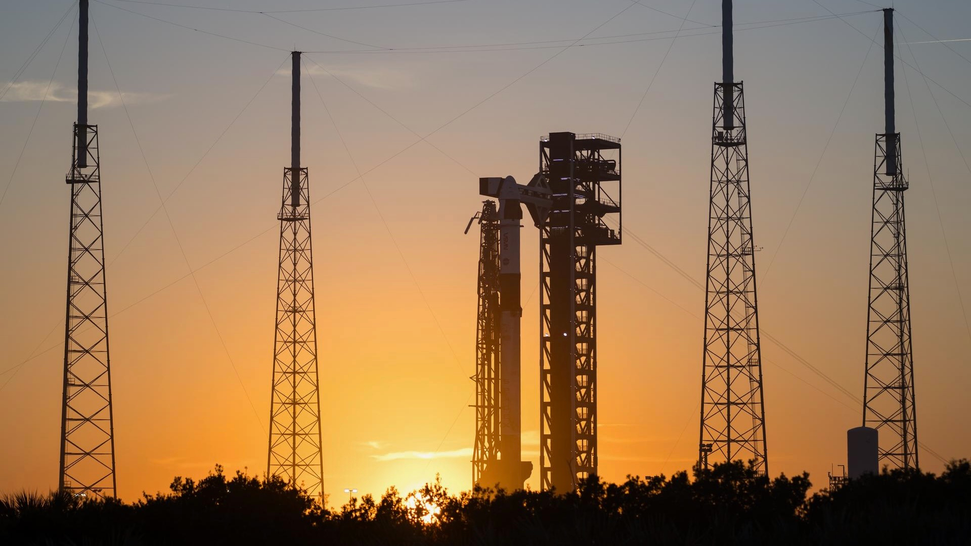 a tall rocket stands on a launch pad with the setting sun in the background