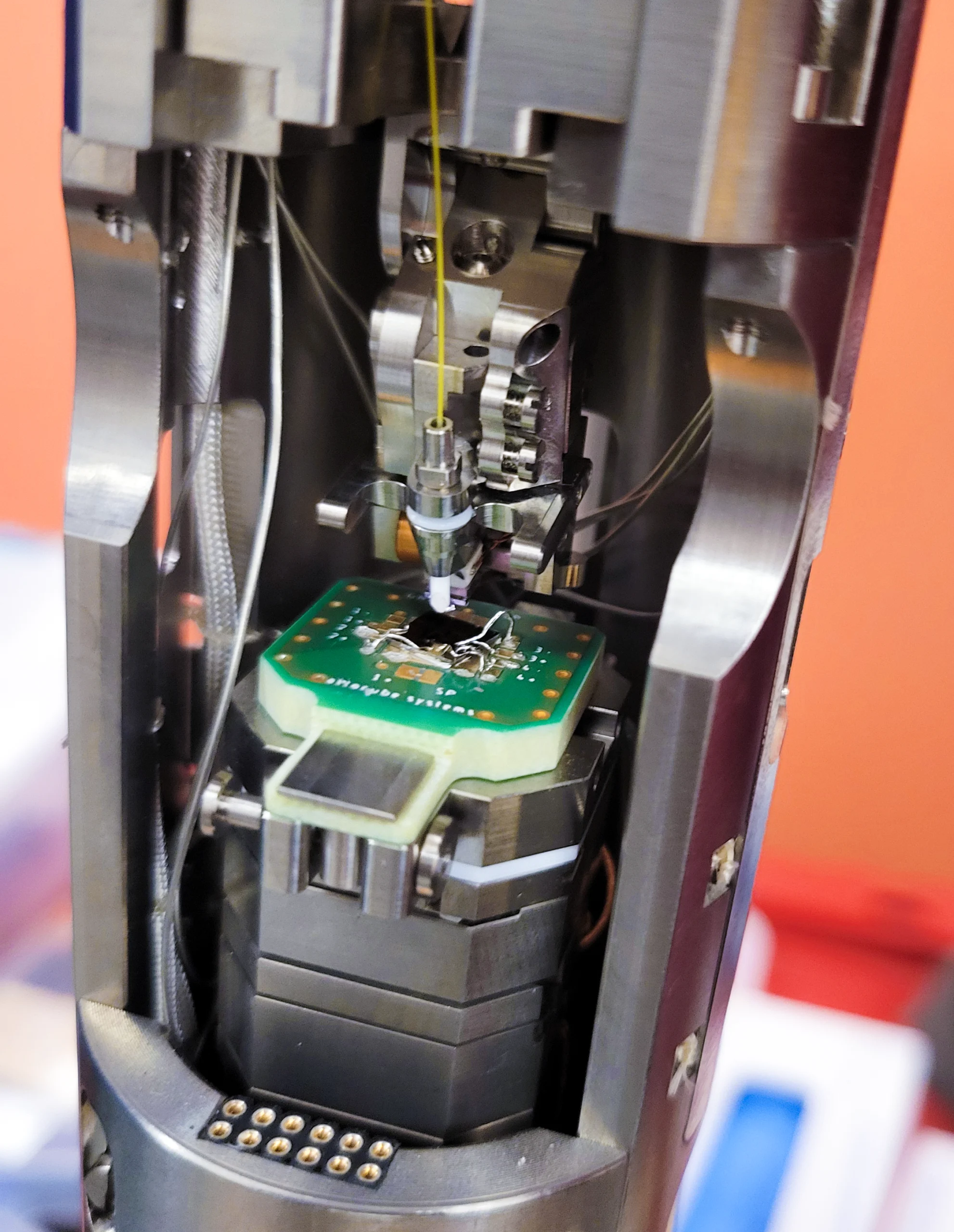 A metallic head hovers above a platform inside a laboratory device.