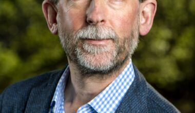 A man in a dark blue suit poses for a profile photo against a blurred green background