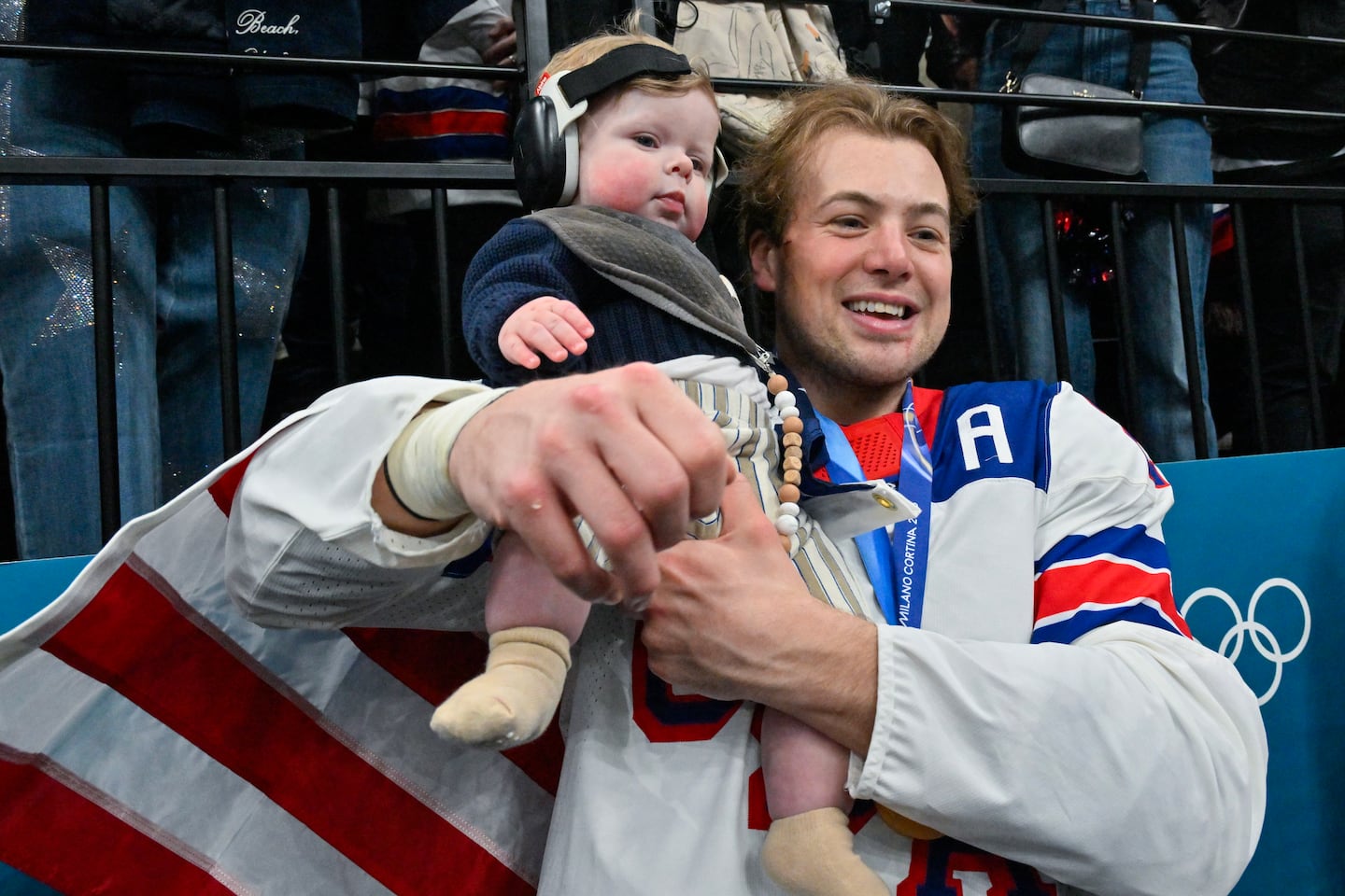 A flag-draped Charlie McAvoy celebrates his new gold medal with his child. 