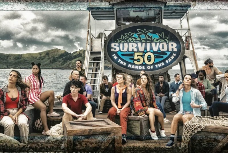Group of contestants from Survivor 50, titled "In the Hands of the Fans," seated on a boat with a scenic backdrop of hills and cloudy skies. The cast showcases diverse personalities and styles, reflecting the competitive spirit of the reality show.