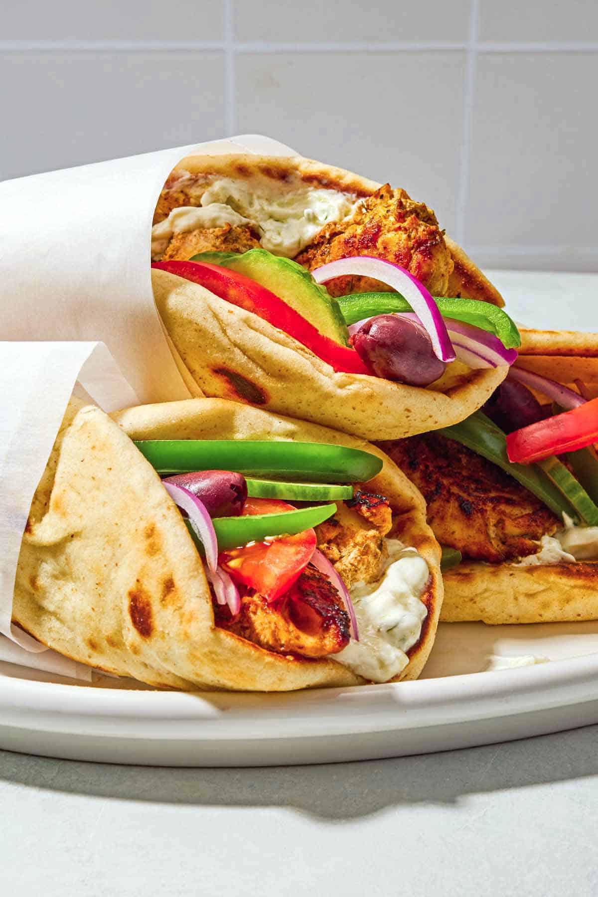 Three chicken gyros on a plate, each one wrapped in parchment paper.