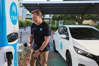 A CSIRO staff member prepares to plug a charger into a white electric vehicle at a solar-powered charging station.
