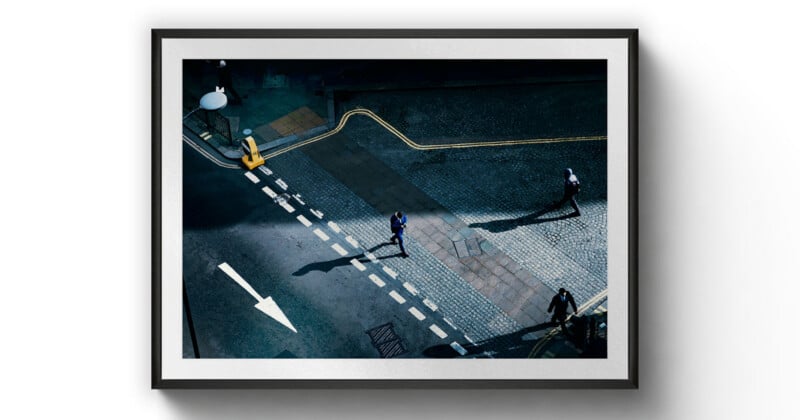 Framed photo of a city street seen from above, showing three people walking on pavement and casting long shadows. A white arrow points forward on the road, and yellow lines curve along the sidewalk.