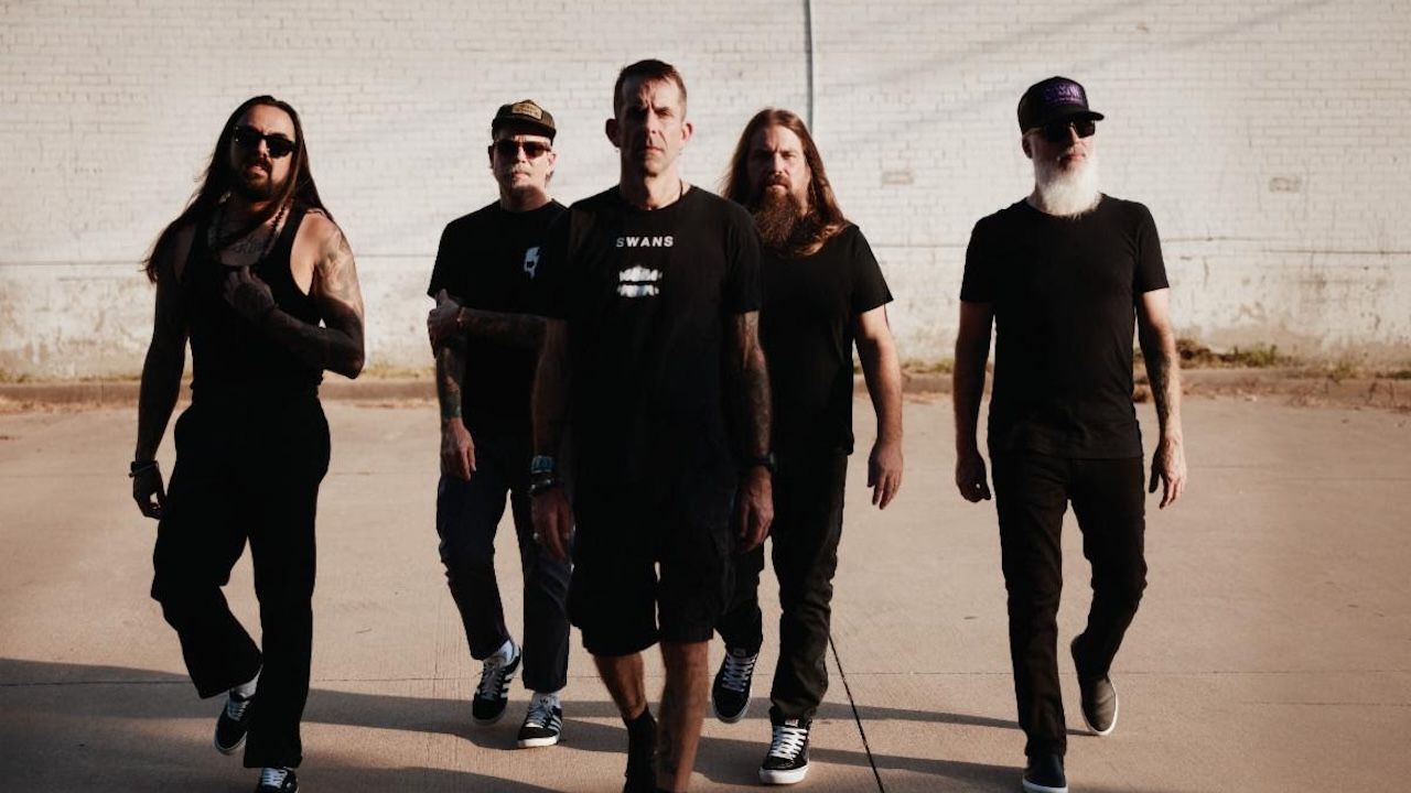 A press shot of Lamb of God walking towards the camera against a plain concrete background