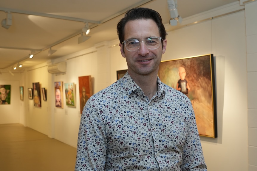 Tim stands and smiles, artworks on the walls behind him.