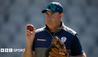 Derbyshire head of cricket Mickey Arthur wearing a baseball glove and holding a cricket ball in the other hand
