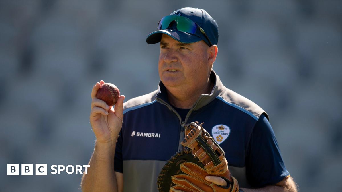 Derbyshire head of cricket Mickey Arthur wearing a baseball glove and holding a cricket ball in the other hand