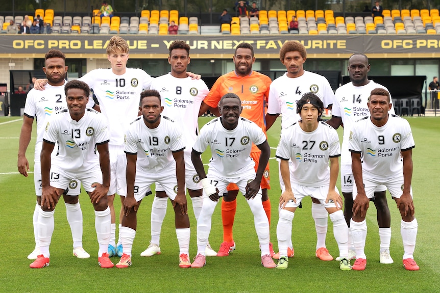 A football team gather in the centre of the field for a pre-game photo.