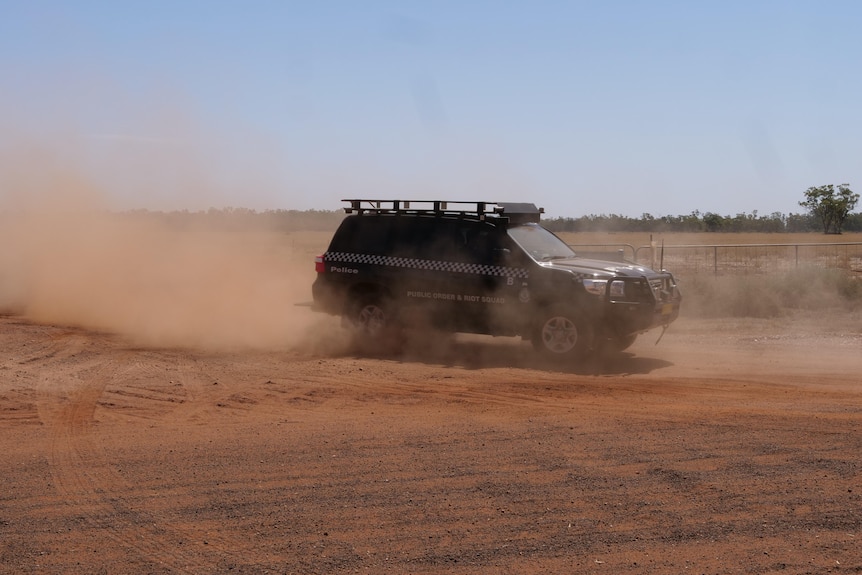 Police riot squad car drives through red dirt