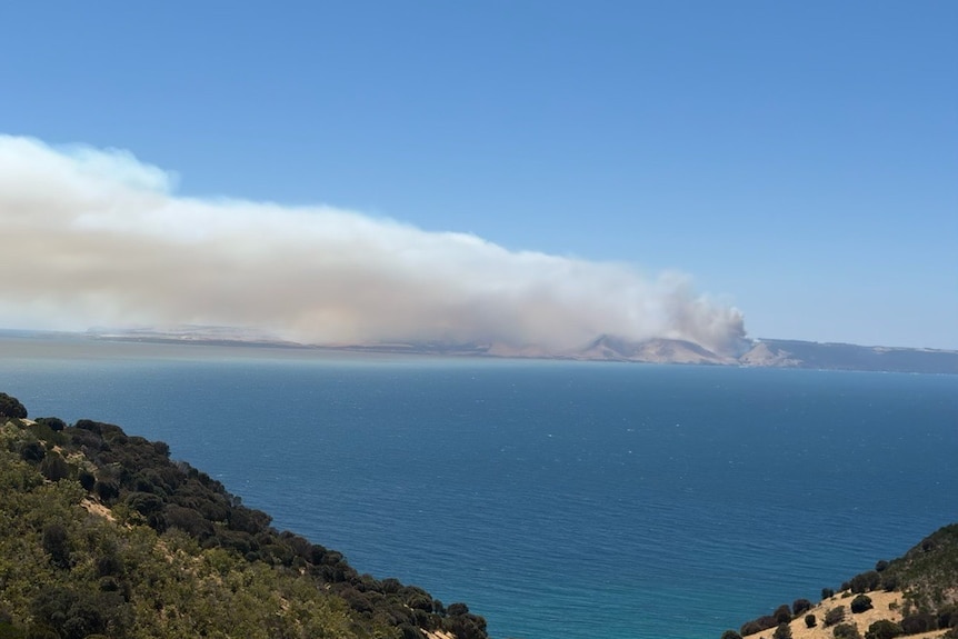 Smoke billows across a blue sky from a land mass in the distance.