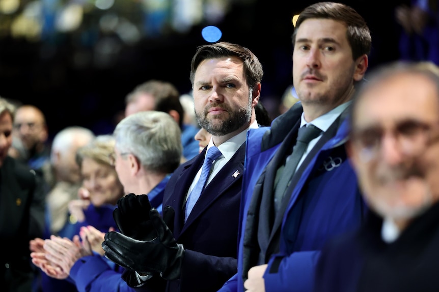 JD Vance is clapping while looking stern in a line of people