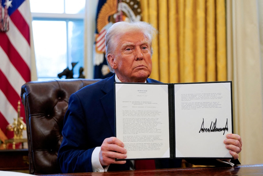 Trump holds a folder with papers that have his signature.