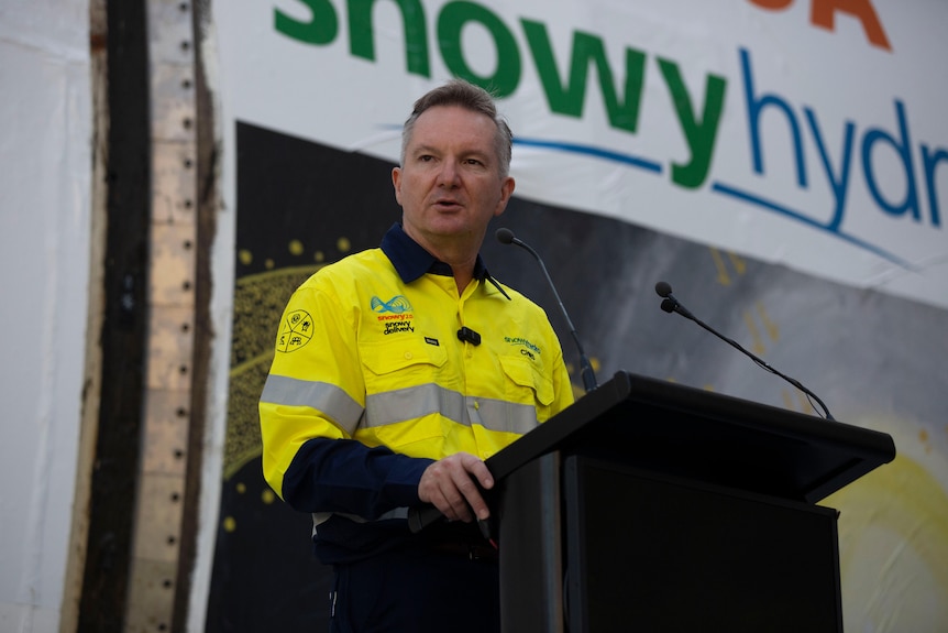 A man in a yellow construction outfit, speaking at a lecturn.