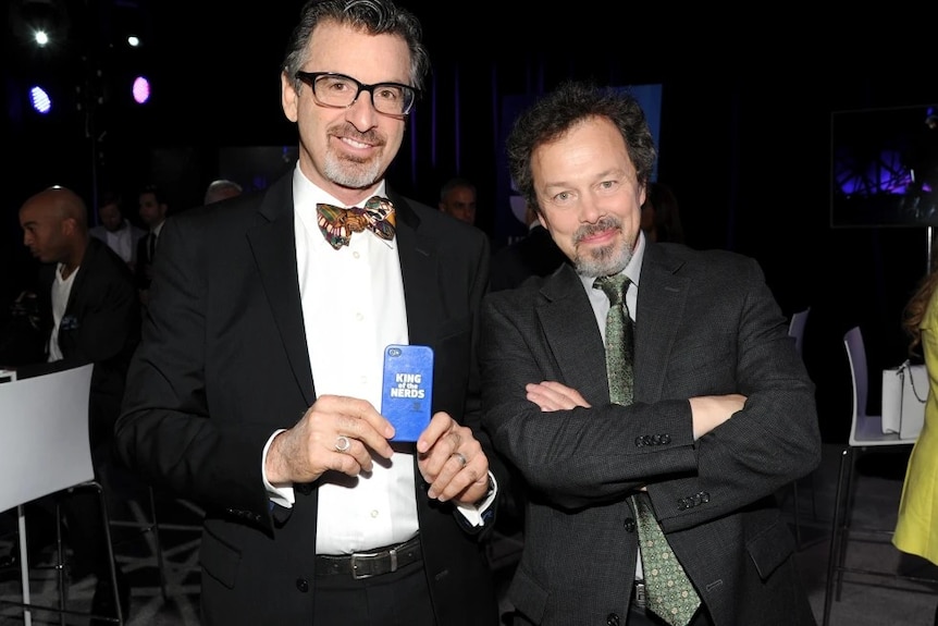 Two men in suits with one holding a phone case with the title "king of nerds"