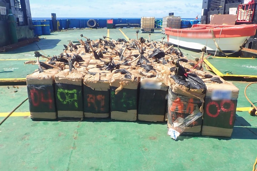 Rows of large, numbered brown rectangle-shaped parcels on board a vessel.