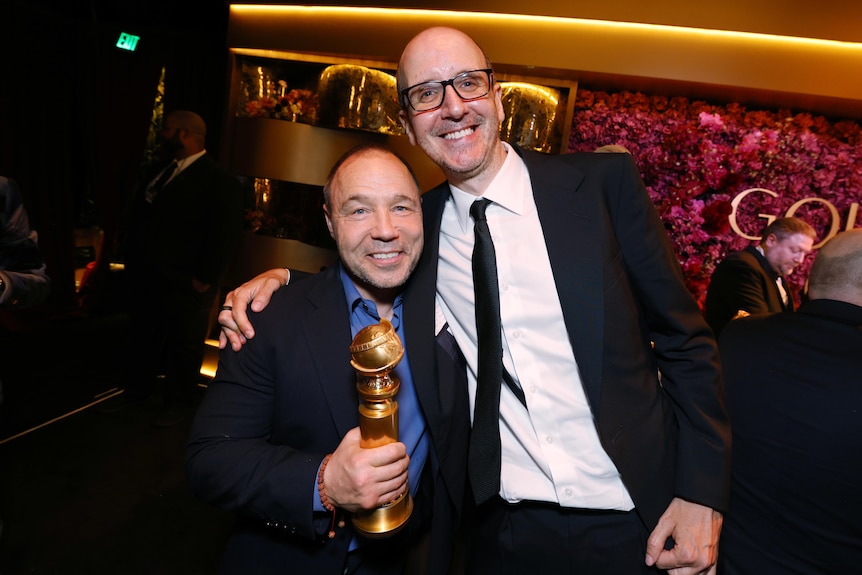 Jack Thorne, 47, bespectacled, in a suit, smiles, arm around Stephen Graham, 52, who is grinning and holding a Golden Globe.