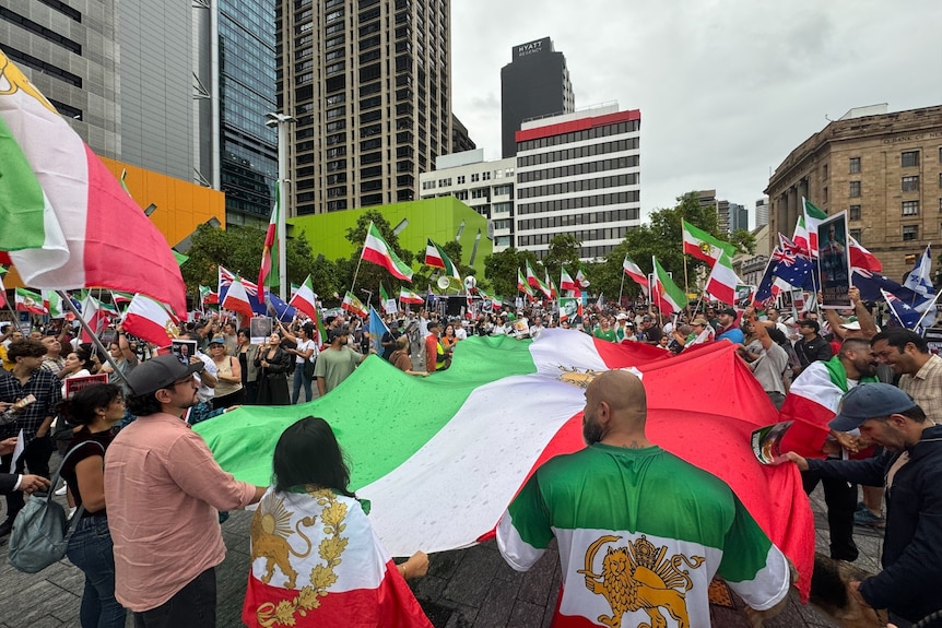 A large Iranian flag is carried among hundres of protestors